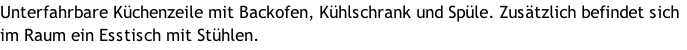 Unterfahrbare Küchenzeile mit Backofen, Kühlschrank und Spüle. Zusätzlich befindet sich im Raum ein Esstisch mit Stühlen.
